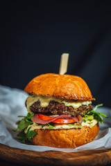 Homemade grilled beef burger with blue cheese and rucola served on wooden plate on dark background