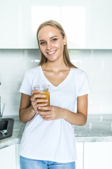 Attractive young woman holding a glass of orange juice while standing in the kitchen