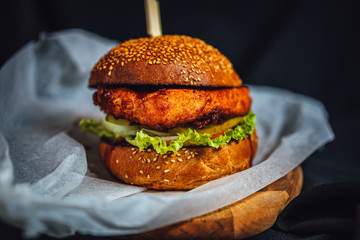 Homemade crispy chicken fillet burger with tomatoes, pickled cucumbers, and bbq souce on dark...