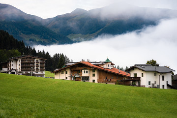 Alpine village in the fog surrounded by forest and mountains. In the background, mountains and fog