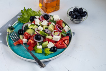 Naklejka na ściany i meble Greek salad. Diced tomatoes, cucumbers, feta cheese, olives. Rings of red onion. Food for vegetarians. Festive and New Year's dish. On a light background. Copy space. 