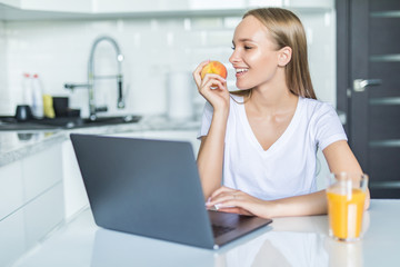 Young woman with green apple and laptop sitting in the kitchen