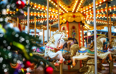 Сarousel horses to traditional Christmas market. Outdoor fair on winter day. View through the frost pine branch. Happy new year. Festive street decor in winter holidays.