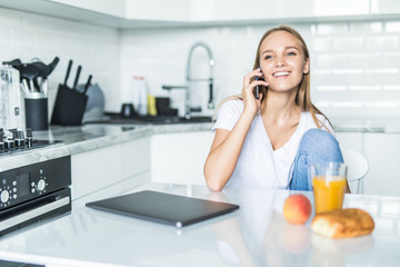 Young woman talking on mobile phone while using laptop in kitchen at home