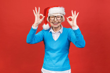 Senior aged grey-haired woman wearing Christmas Santa hat over isolated red background very happy and excited, having fun, smiling.