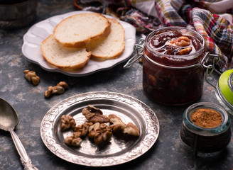 Jar of homemade plum jam marmalade with walnuts and french bread on the kitchen dark table. Healthy dessert snack recipes concept. 