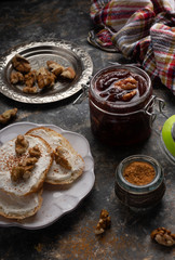 Jar of homemade plum jam marmalade with walnuts and french bread on the kitchen dark table. Healthy dessert snack recipes concept. 