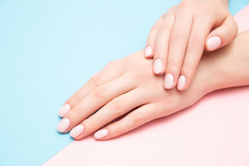 Beautiful female hands with stylish nail manicure gel polish on pink and blue background, top view. Skin care concept
