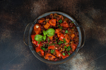 A traditional Caucasian dish, lobio of red beans with vegetables and herbs on a tin tray stands on a concrete table. Vegetarian stew of beans, paprika and herbs. Horizontal orientation. Top view.
