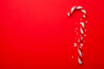 Broken Christmas candy cane on red background.  Top view with space for text. Minimal composition