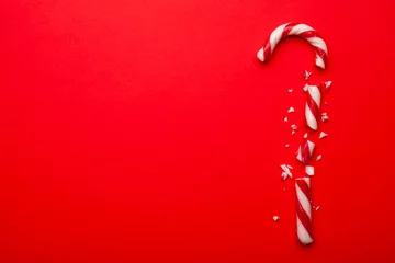Tuinposter Broken Christmas candy cane on red background.  Top view with space for text. Minimal composition © Random435