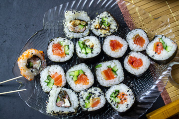 red fish sushi with rice filling, on a serving plate on a black background, top view