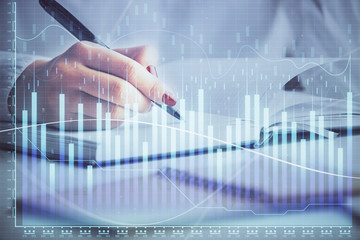Multi exposure of woman's hands making notes with forex graph hologram. Concept stock market...