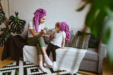 mom and daughter are playing at the beautician, sitting on the couch are painted with makeup brushes - 304802360
