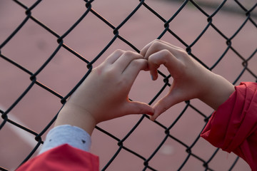 the girl and her mum hold the stadium iron wire mesh and look at the playing people.