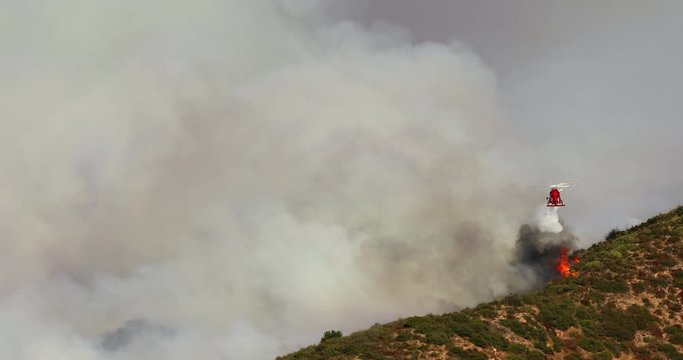 November 9, 2019. Footage of a red helicopter dropping the water against the background of thick smoke from wildfire. Hollywood hills. Warner brothers wildfire. Los Angeles County. 4K
