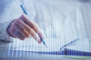 Financial forex graph displayed on hands taking notes background. Concept of research. Double exposure