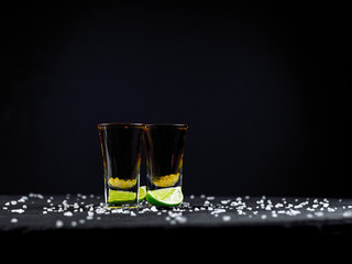 Two shots tequila gold with juicy lime and sea salt on a dark background