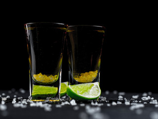 Two shots tequila gold with juicy lime and sea salt on a dark background
