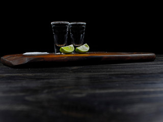 Two tequila silver shots with fresh lime and sea salt on wooden board and dark background