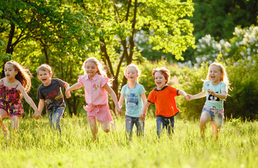 A group of happy children of boys and girls run in the Park on the grass on a Sunny summer day . The concept of ethnic friendship, peace, kindness, childhood