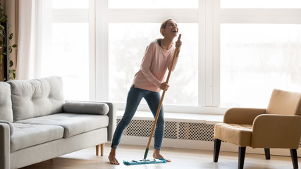 Happy young woman have fun dancing cleaning home