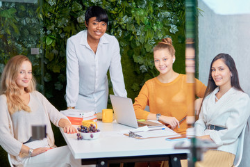 Fototapeta premium Portrait of attentive caucasian listeners and african business coach looking at camera, team leader and young business ladies in modern office