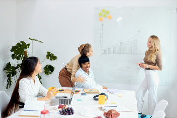 Young beautiful business coach teacher team leader represent her business strategy to co-workers in white office, multi-ethnic group of listeners