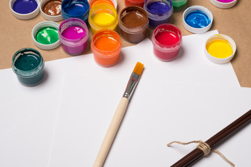 Paints for painting with brushes on a white sheet. Acrylic paints in tubes. Old paint in bottles. Paint brushes for painting and a blank white sheet of paper for text.