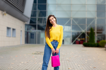 Fototapeta premium Happy brunette woman dressed in yellow sweater, with shopping bags enjoying in shopping. Shopping, lifestyle concept