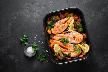 Salmon. Baked salmon fish steaks with vegetables, broccoli, carrot and onion on black background,...