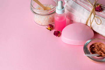 Face care cosmetics with organic scrub, mask, soap and rose oil on pink background with a towel