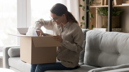 Happy young woman unpacking cardboard box at home