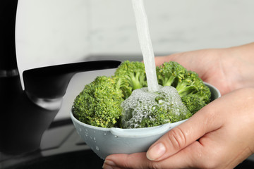 Woman washing fresh green broccoli in kitchen sink, closeup