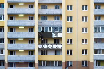 Fototapeta premium Large Building Site. Workers Building New House, install Windows, Wall Insulation, Balcony. Industrial Building Construction. Two workers perform repairs to the facade of the building at a height of
