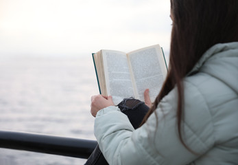 Obraz premium Woman reading book near river on cloudy day