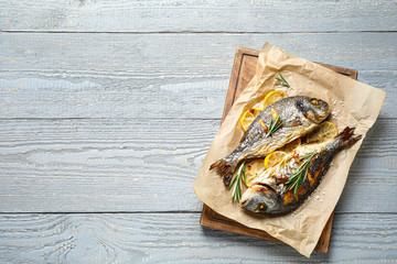 Delicious roasted fish with lemon on grey wooden table, flat lay. Space for text