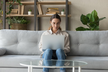 Millennial woman sit on couch at home using laptop