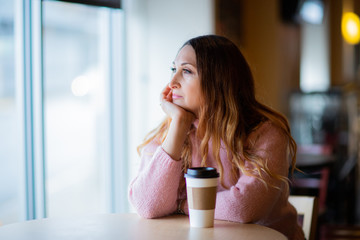 White female sitting in coffee store, shop close to window. happy, beautiful, dreaming woman in sweater 
