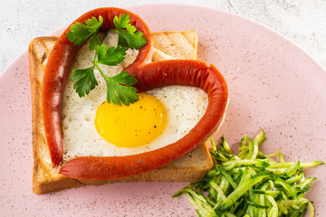 Scrambled eggs in the form of heart on a white plate with sausages, sourdough toast isolated on white marble background. Homemade food. Tasty breakfast. Selective focus. Hotizontal photo.