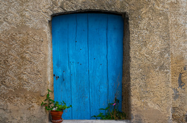Fototapeta na wymiar Old building in France. Wall with blue door and flower pot. Building with beautiful old architecture. Old door on old wall.