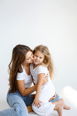 Happy mom and daughter are hugging and spending time together on a white wall background. Happy family concept