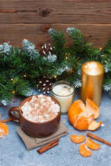 Cup of cocoa with marshmallow, cinnamon rolls, tangerine, burning candles and christmas tree garland near wooden wall. 