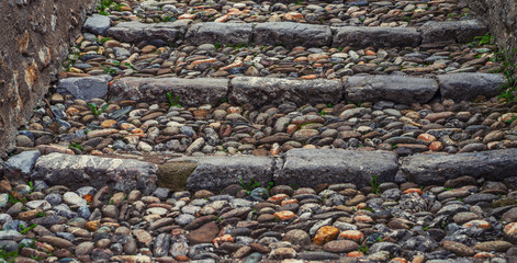 An old open outer stone staircase. Stone steps of the old staircase with traces of weathering and destruction. An ancient stone staircase, ancient broken worn steps.