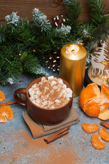 Cup of cocoa with marshmallow, cinnamon rolls, tangerine, burning candles and christmas tree garland near wooden wall. 