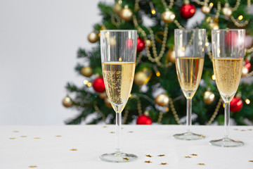 three glasses with champagne or cava on white table with christmas tree in the background