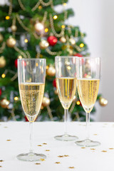 three glasses with champagne or cava on white table with christmas tree in the background