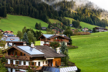 Fototapeta na wymiar Traditional houses with solar panel roof in Austria . Tirol, Mountains, trees, grasses, and forest surrounding. Solar energy in Mountains.