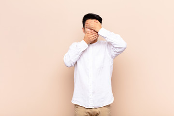 young chinese man covering face with both hands saying no to the camera! refusing pictures or...