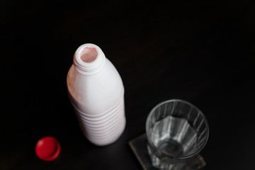 Opened bottle of strawberry or raspberry yogurt standing on black table with glass. Dairy product. Healthy food and drinks concept. Place for text.